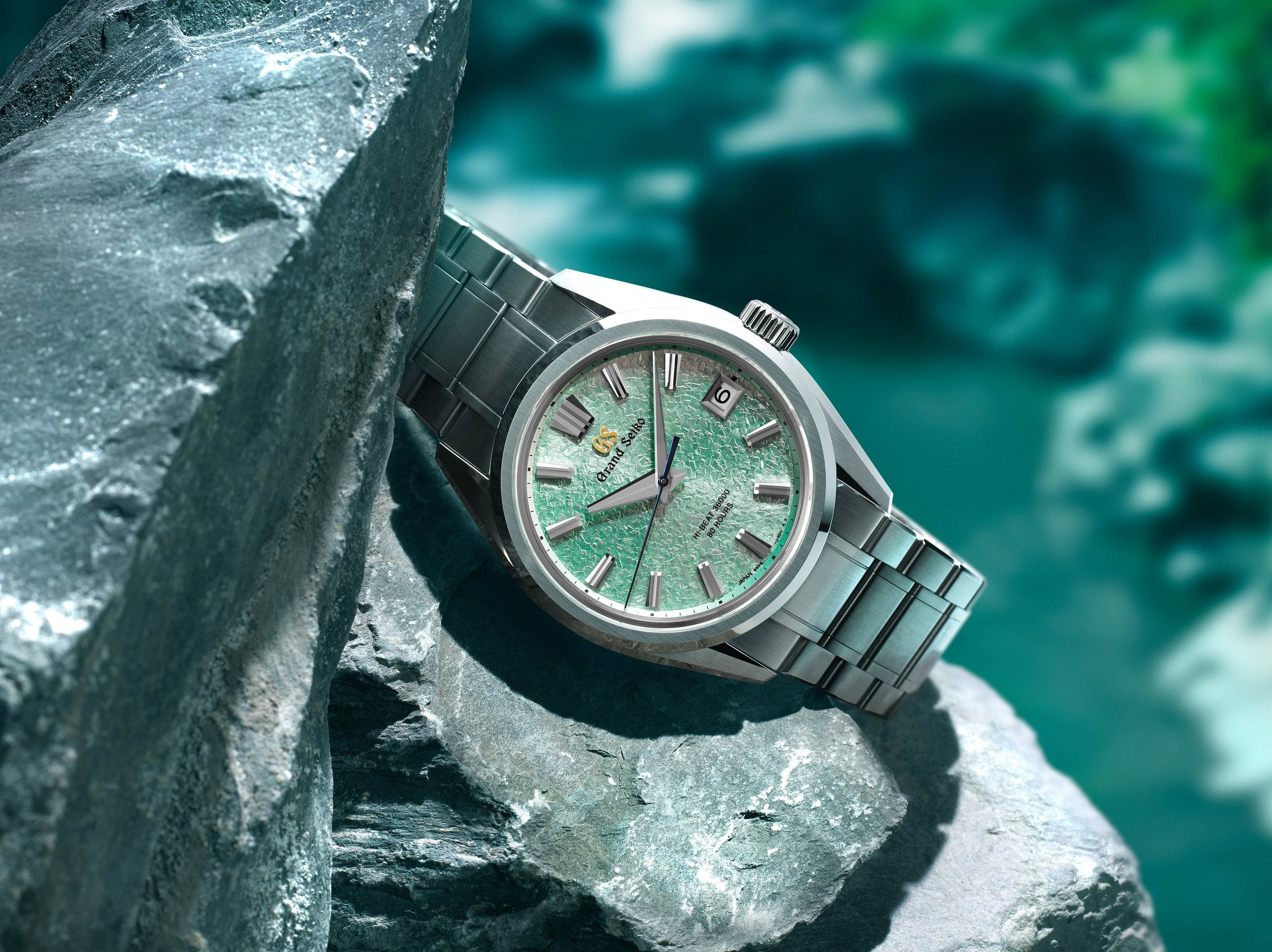 Silver colored Grand Seiko watch perched on the side of rocks in a nature setting.