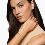 Woman with long dark hair touching her neck against a white background featuring an Open cable bracelet with two blue colors gemstones and mixed metal end caps. 