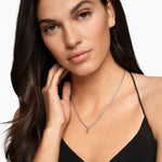 Woman wearing a black top and silver heart shaped necklace with ap pink gemstone on a white background