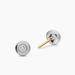 Pair of silver earrings with a diamond in the center on a white background. One earring is turned around so you can see a gold stud. 
