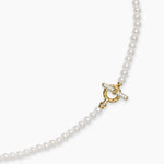 Up close image of a delicate pearl necklace with a gold clasp. Part of the gold clasp features pave diamonds