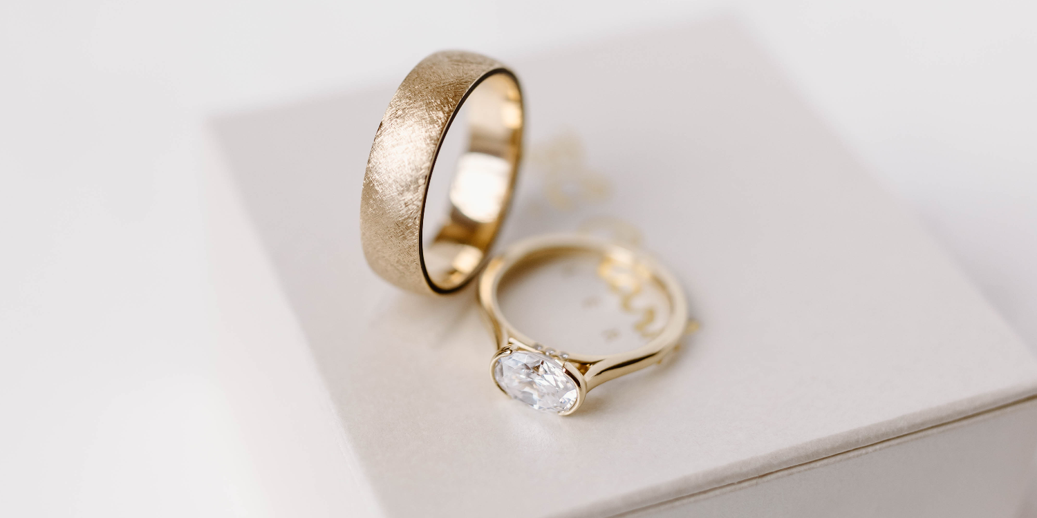 Two gold rings with one featuring a diamond on a white surface | BC Clark Jewelers